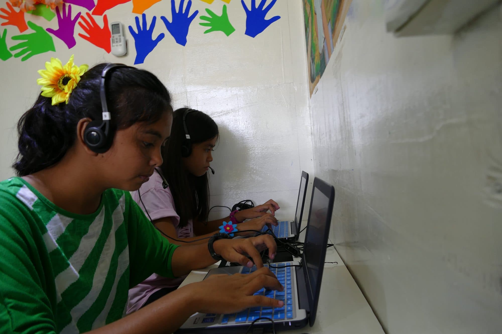 A student with a flower in her hair types at a laptop in the container classroom